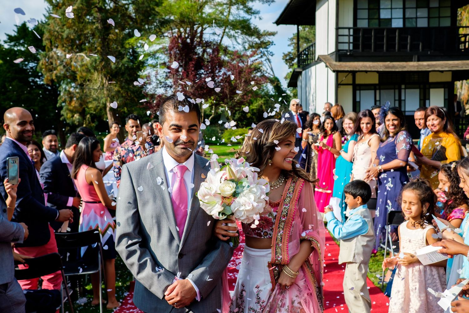 Wedding party and guests line up outdoors against modern building backdrop.