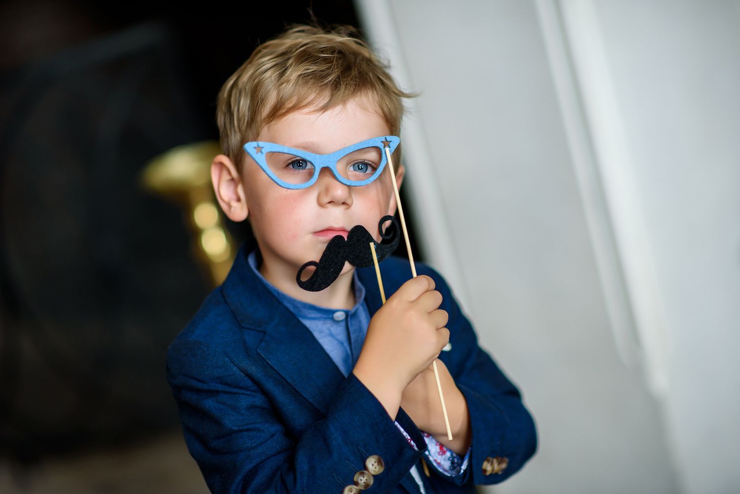 Young attendant in blue glasses and suit poses with prop at formal event.