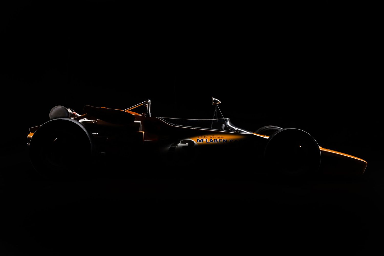 Silhouette of race car against dark background with orange accent lighting.