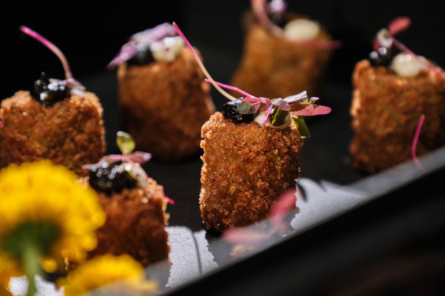 Crispy fried appetizers garnished with edible flowers and microgreens served on a dark slate platter.