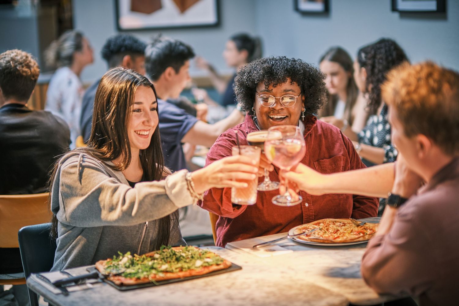 Friends sharing pizza and drinks at a restaurant table with warm ambient lighting.