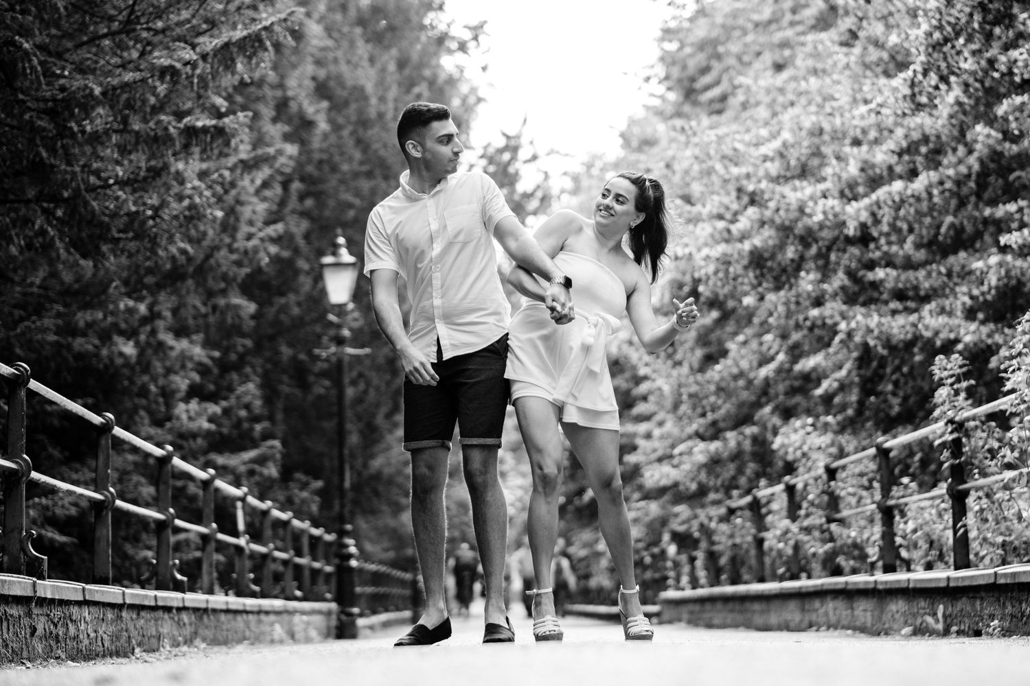 Black and white romantic couple walking on a wooden bridge through lush forest scenery.