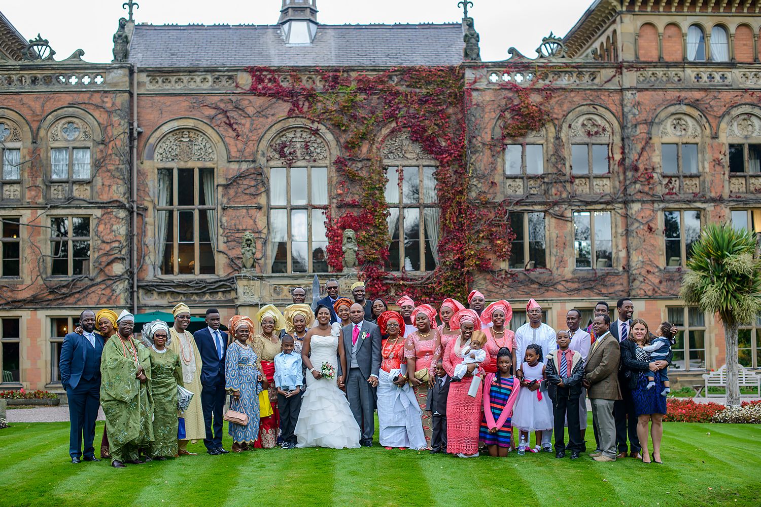 Large wedding party group photo in front of grand historic stone building.