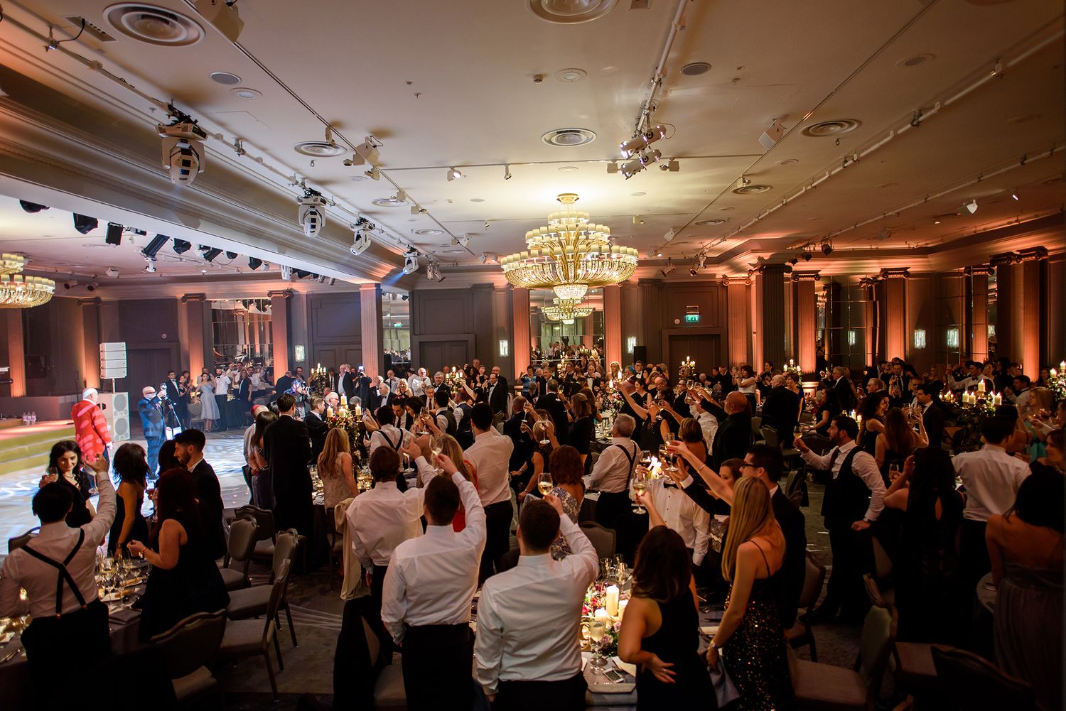 Large wedding reception crowd gathered in an elegant ballroom with warm ambient lighting.