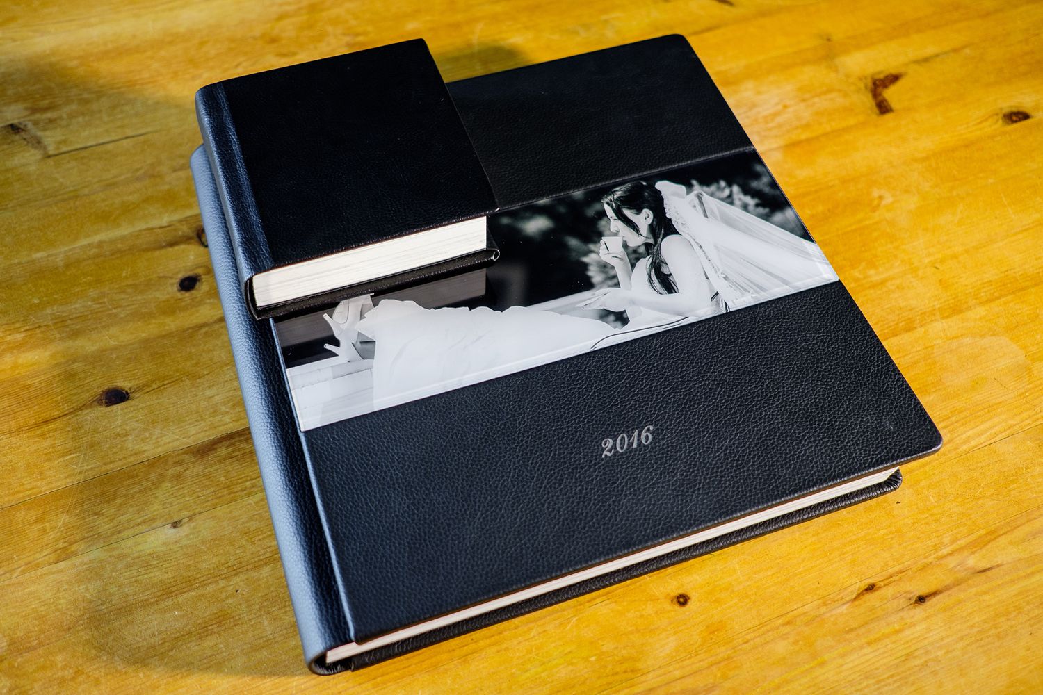 Wedding photo album with black cover resting on wooden table surface.