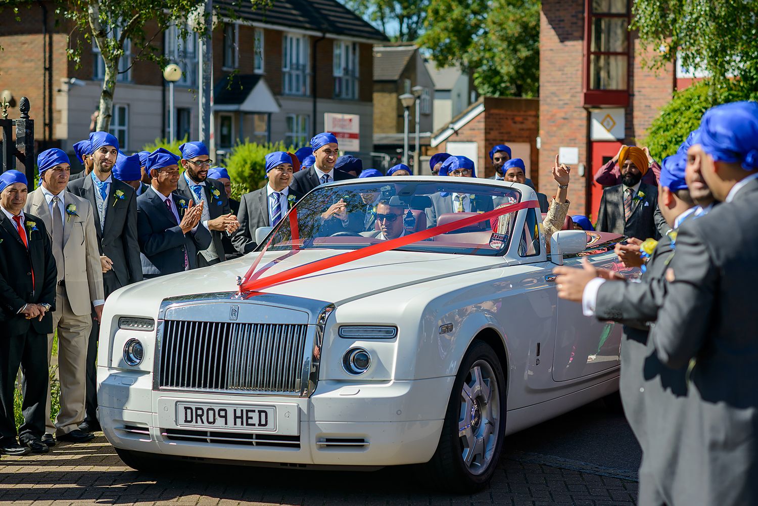 Line of luxury white wedding cars parked along street during daytime celebration.