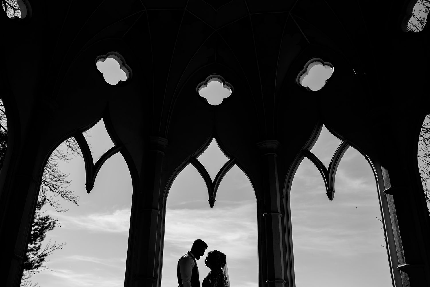 Gothic archways frame silhouetted couple in romantic pose during sunset ceremony.