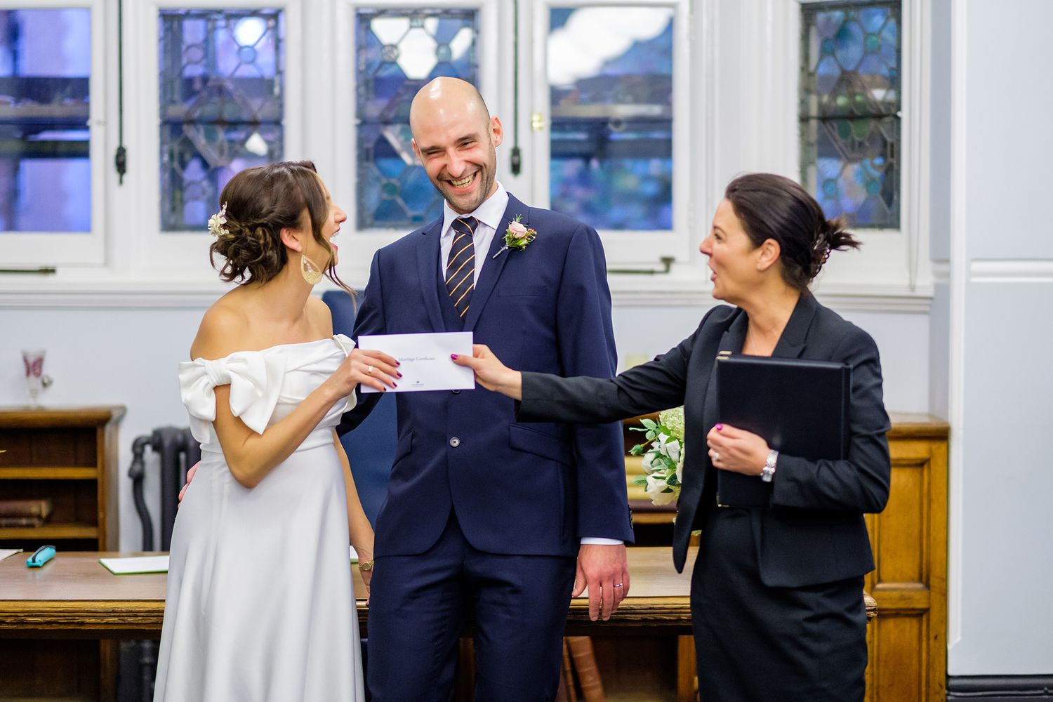 Wedding party stands in front of bright windows during an indoor ceremony.