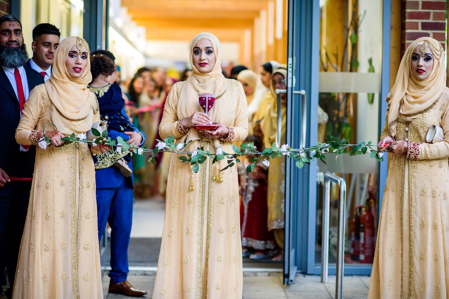 Wedding party in cream colored traditional dresses standing in a bright hallway.