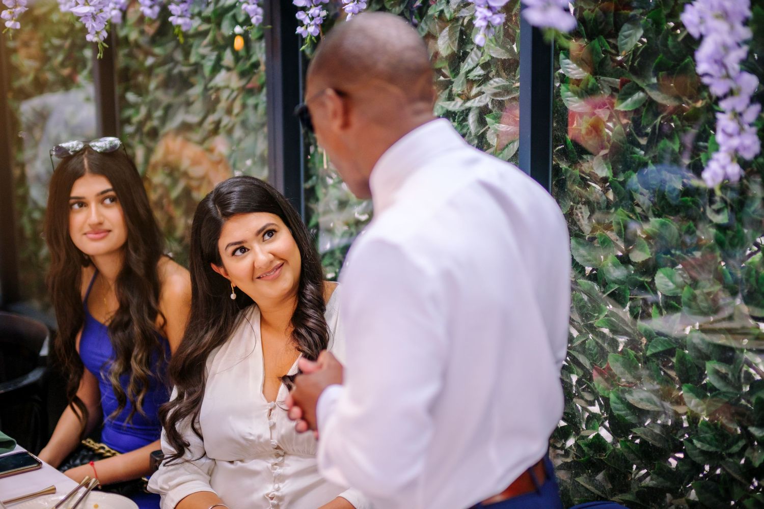 Elegant garden wedding reception with purple wisteria flowers and stone wall backdrop.