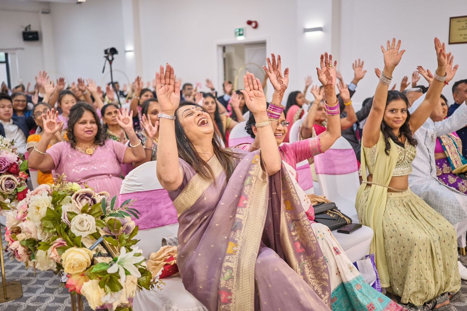 Joyful wedding celebration with guests raising hands in celebration against pink and white decor.