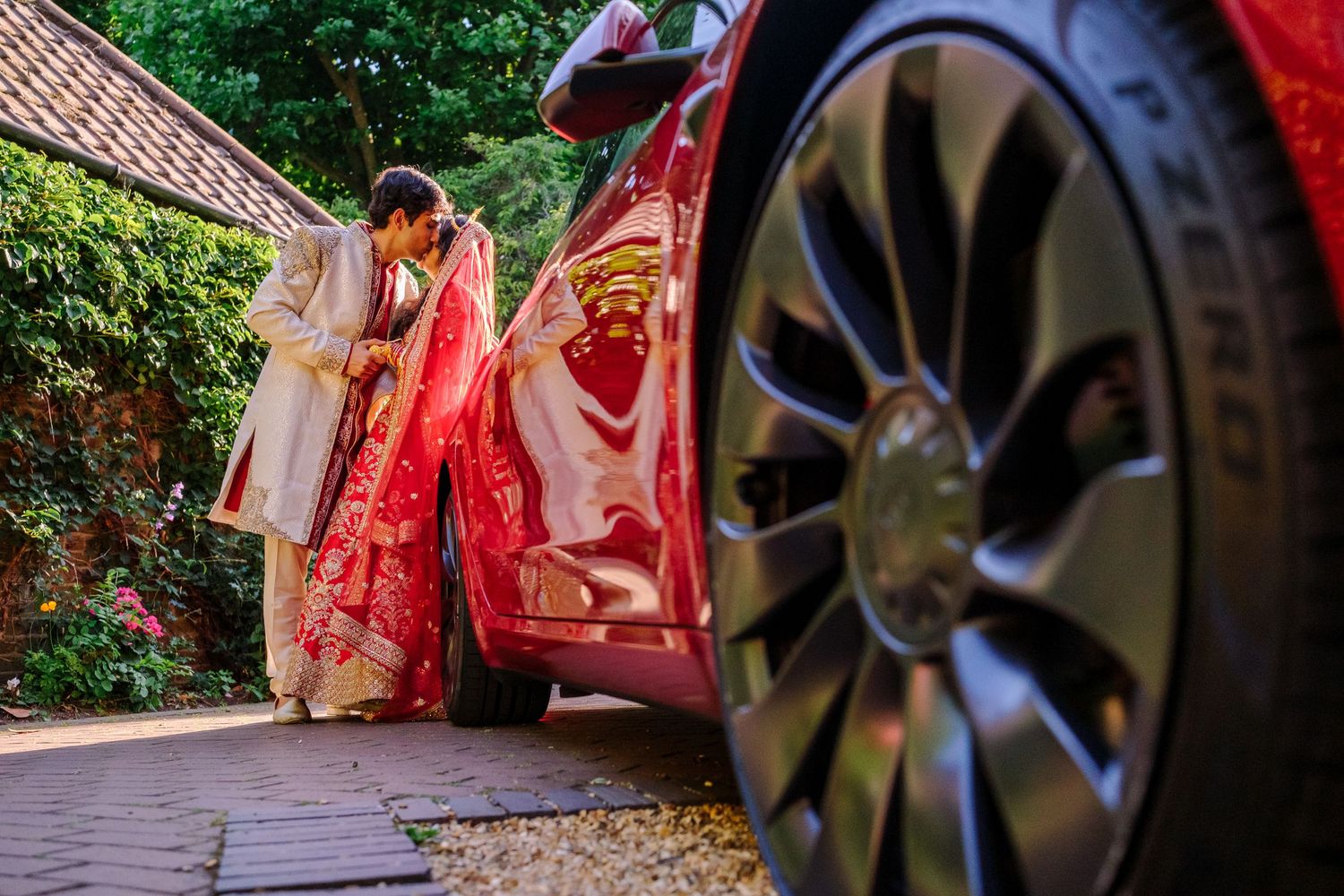 Wedding couple in Indian attire photographed through decorative vintage carriage wheel outdoors.