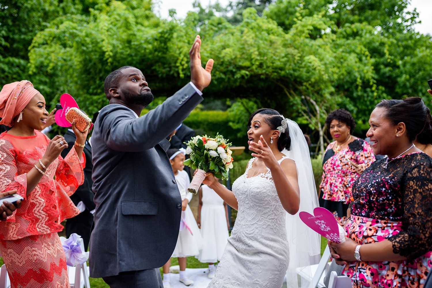 Wedding guests and bridal party dancing and celebrating outdoors surrounded by greenery.