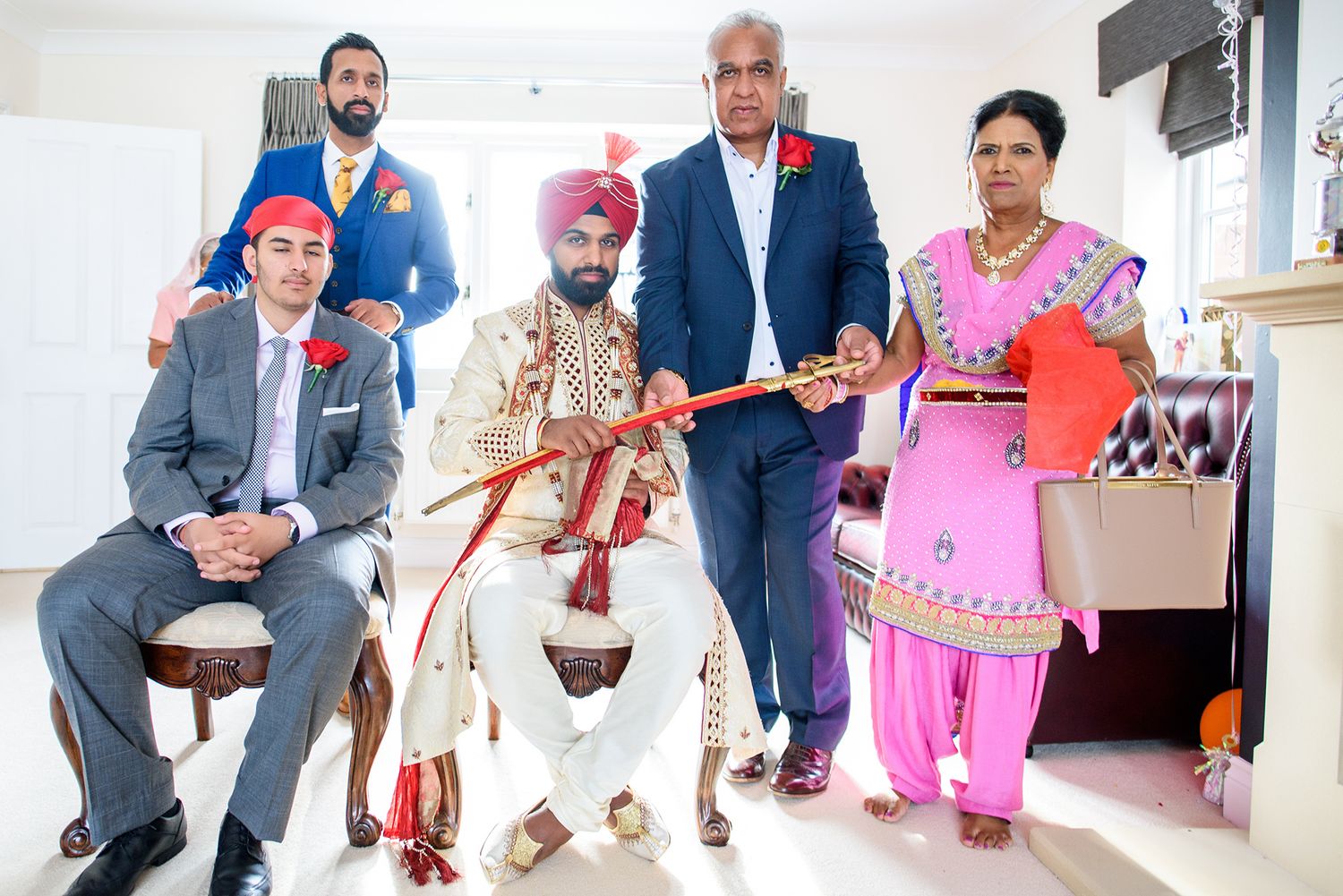 Group portrait showing traditional Indian wedding attire with red and gold color scheme.