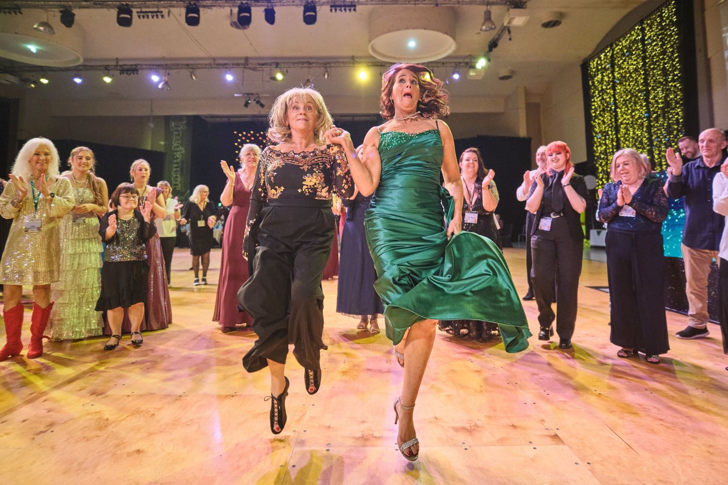 Irish dancers perform synchronized leaps and kicks in emerald green dresses during a traditional dance competition.