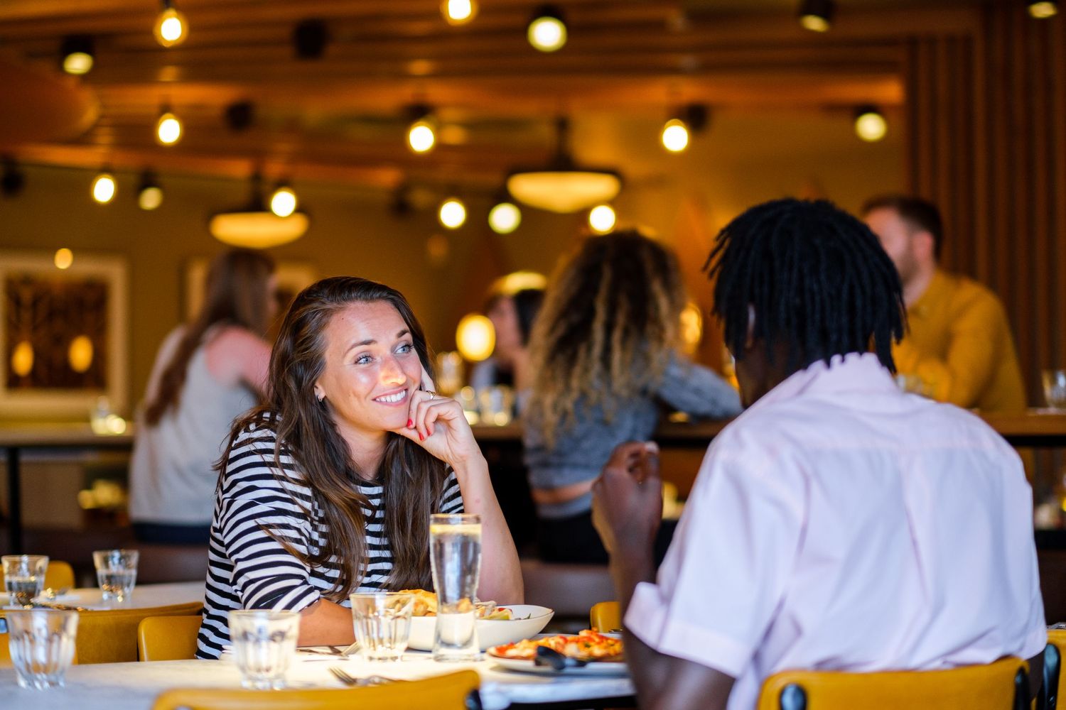 Warm ambient lighting illuminates a restaurant dining room with guests enjoying their meals at tables.