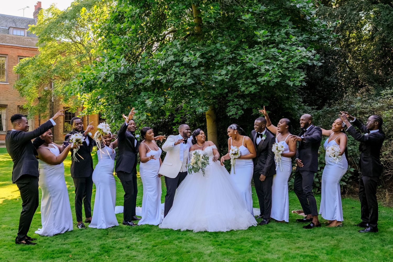 Wedding party lined up outdoors with bridesmaids in white dresses and groomsmen in dark suits.