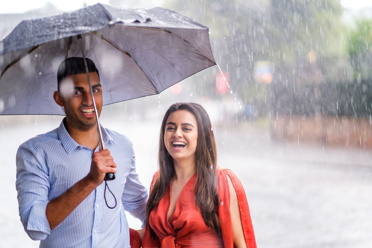 Couple sharing an umbrella and laughing together while standing in the pouring rain.