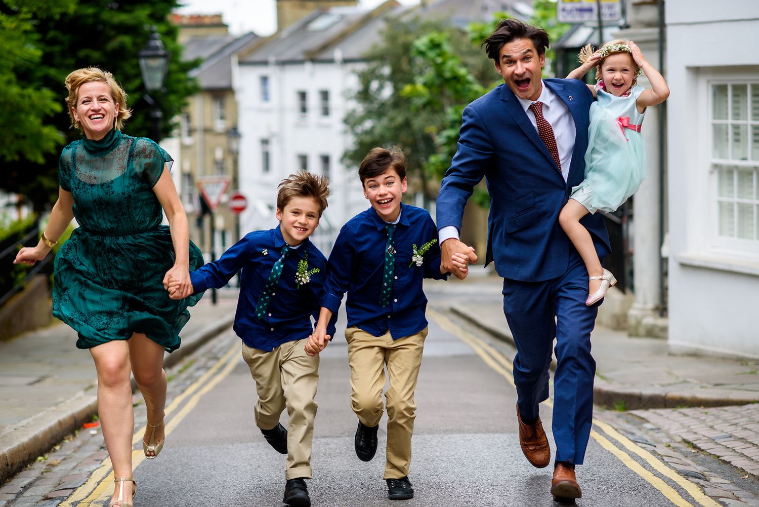 Wedding party runs playfully down cobblestone street in urban setting.