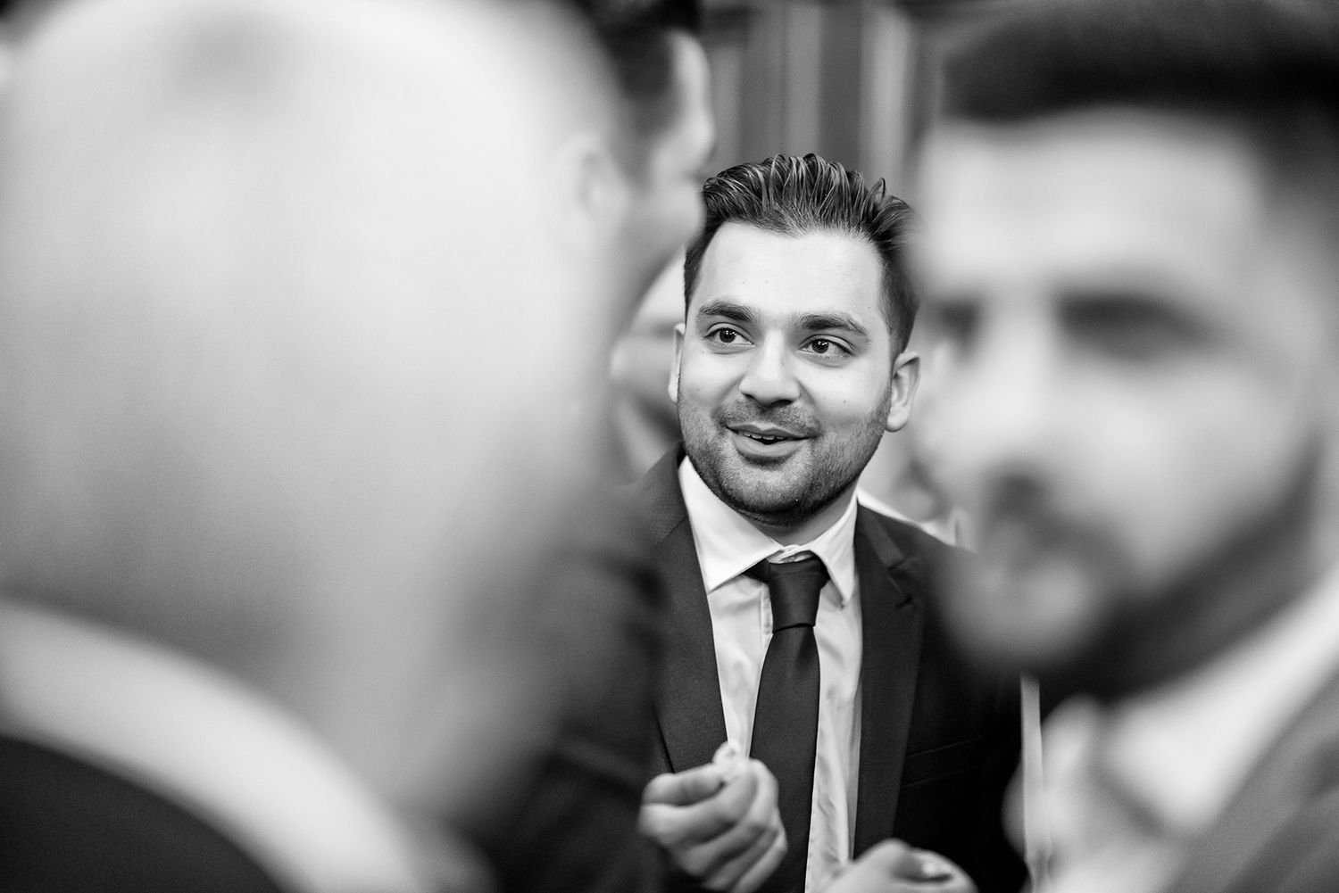 Black and white candid photo of wedding guests in conversation.