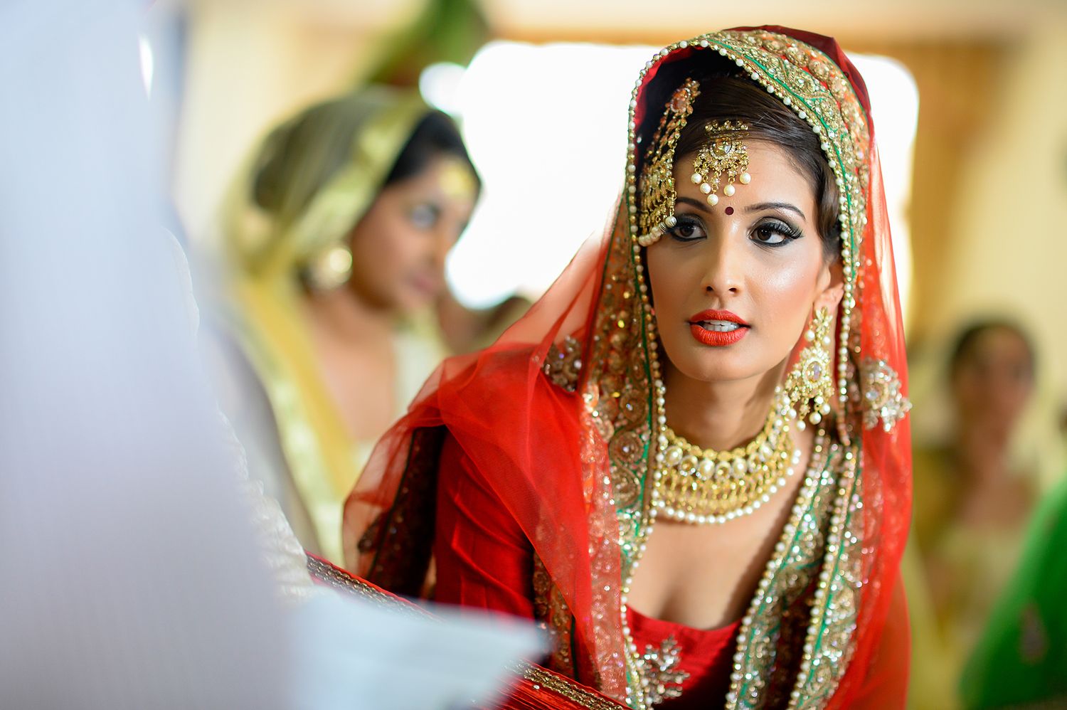Traditional Indian bride wearing ornate red and gold bridal attire with elaborate jewelry and accessories.