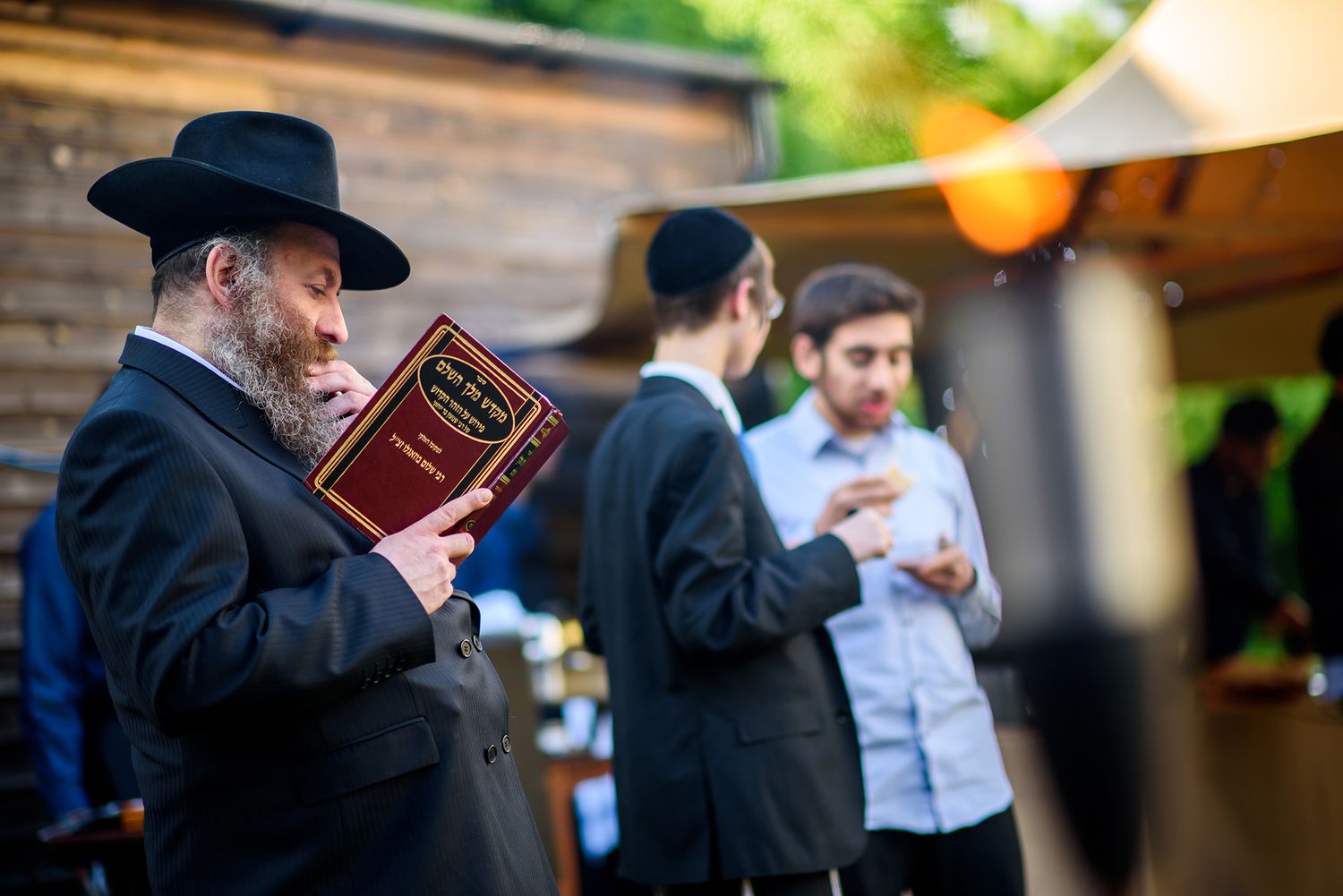 Event attendees hold drinks and socialize in front of a rustic window backdrop.