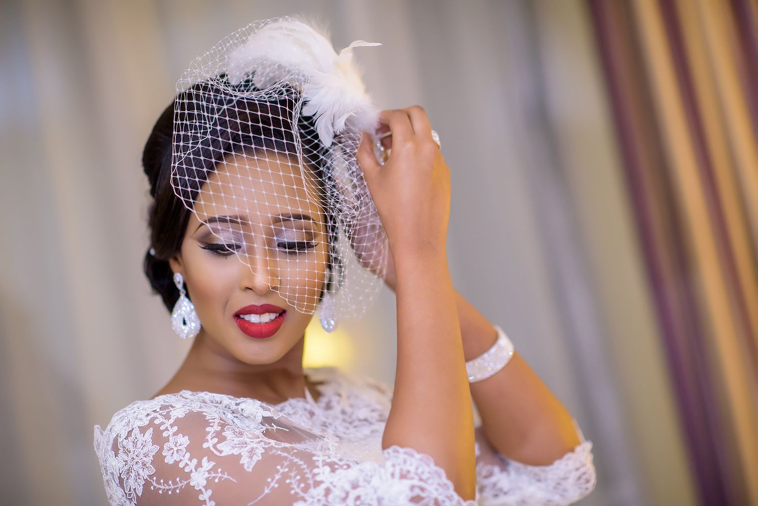Vintage-inspired bride wearing lace gown and birdcage veil in soft lighting.