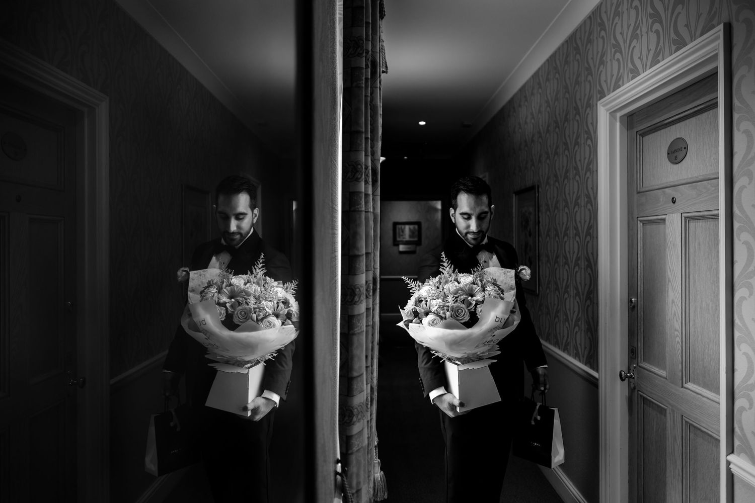Artistic black and white shot of someone holding flowers reflected in a mirror in a hallway.