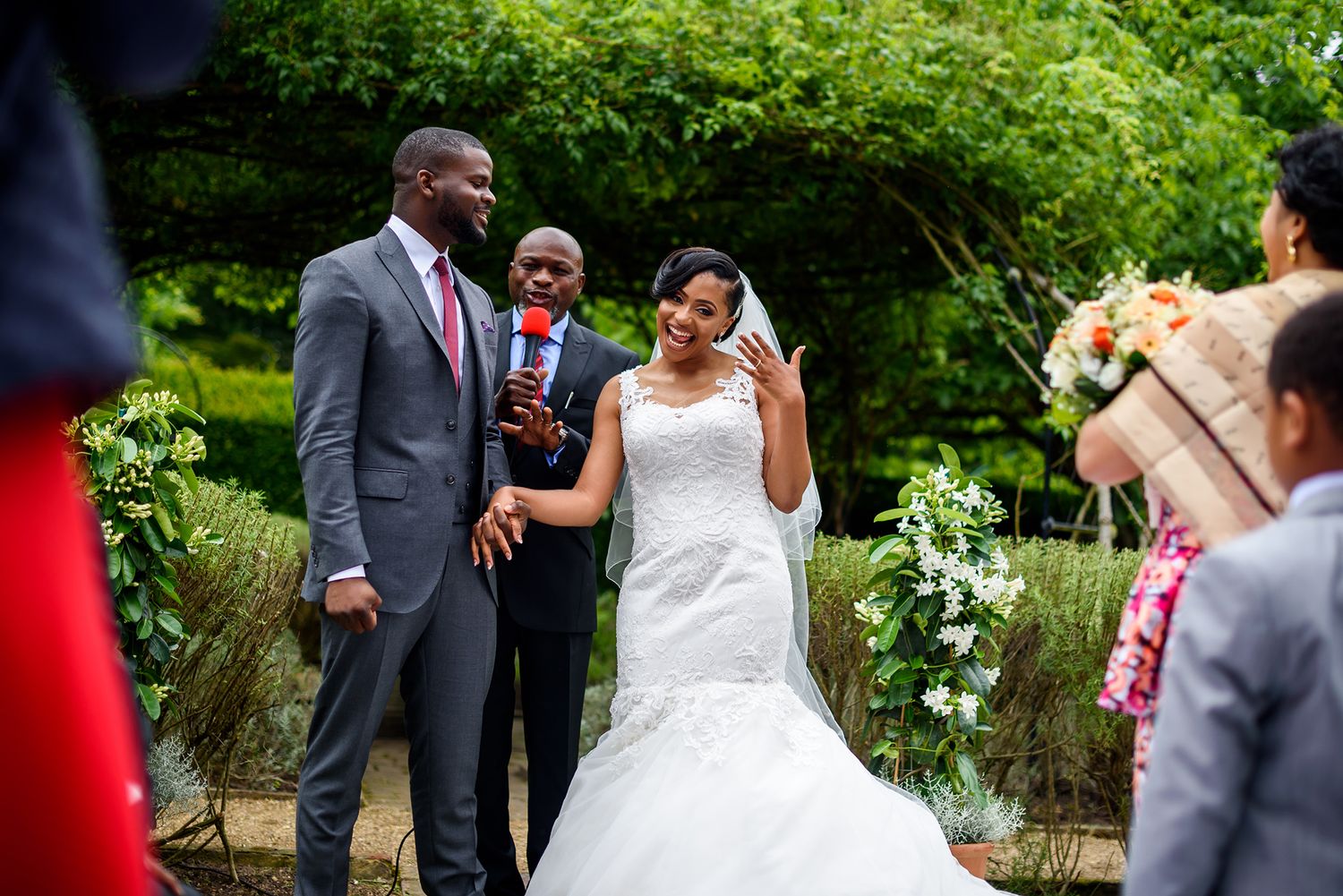 Wedding ceremony taking place in a beautiful green garden setting with guests looking on.