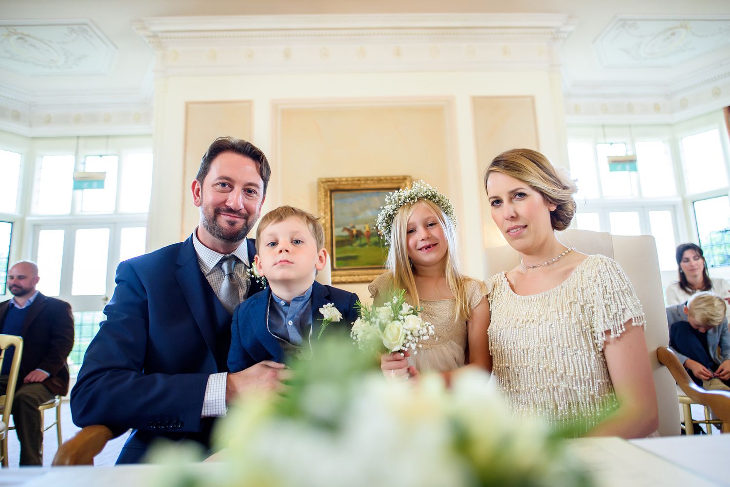 Wedding guests gather intimately at an elegant indoor venue with white decor and floral arrangements.