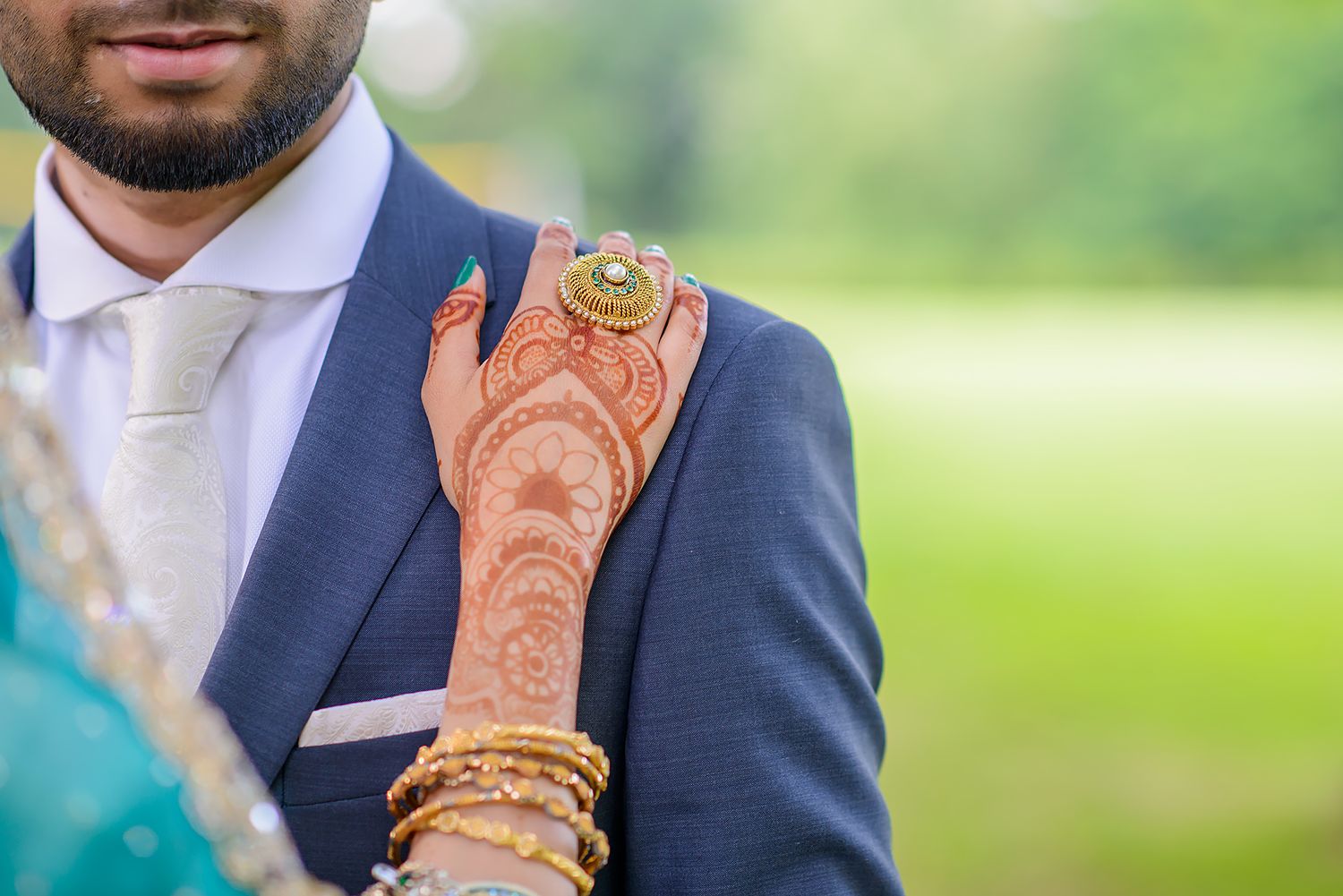 Detailed shot of groom's navy suit and bride's henna-adorned hands with gold bangles.