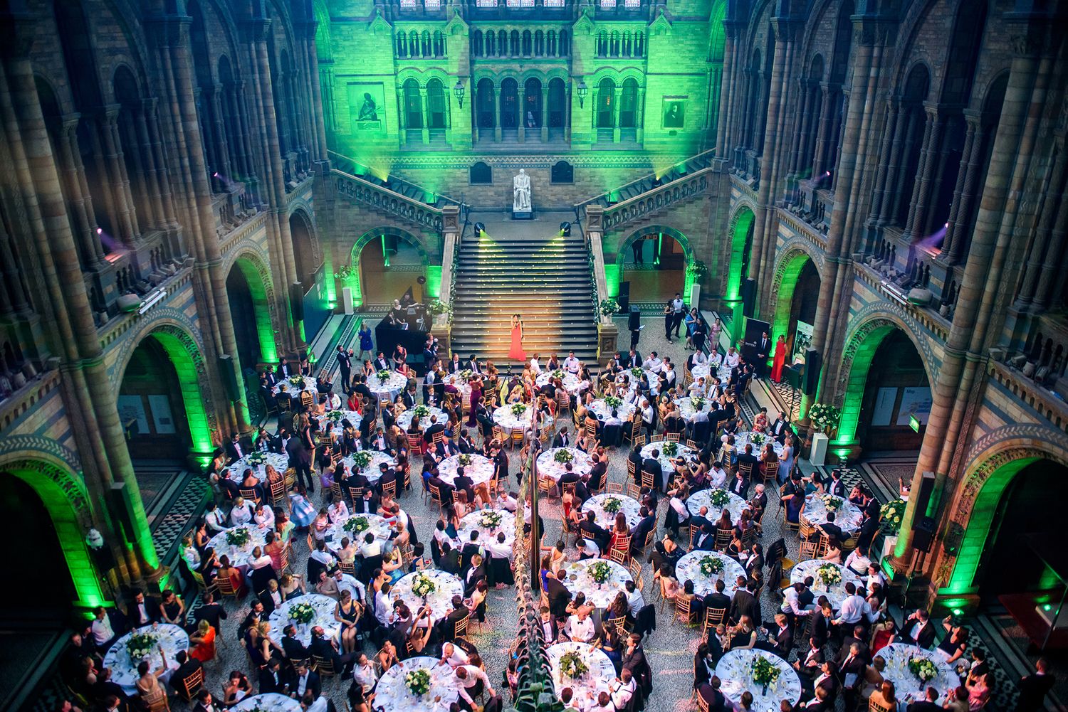 Grand hall filled with guests at formal dinner event with dramatic green architectural lighting.