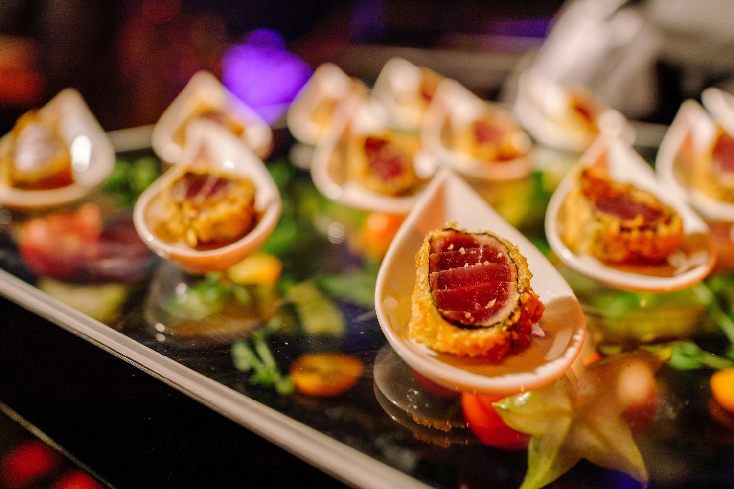 Elegant appetizer bites with vibrant toppings displayed in rows on a sleek serving platter at an upscale event.