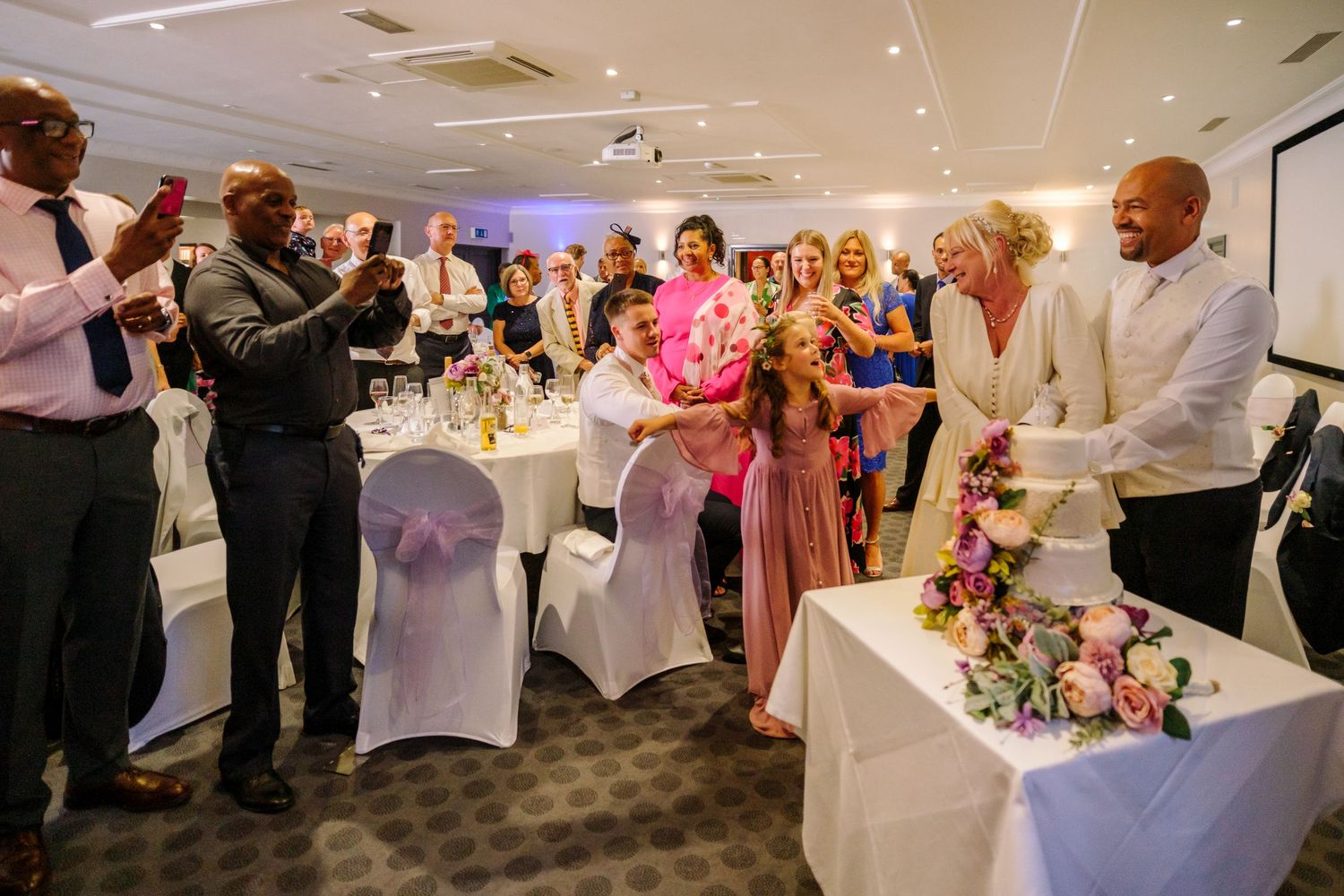 Wedding reception venue decorated with white chairs and pink floral centerpieces in an elegant indoor setting.