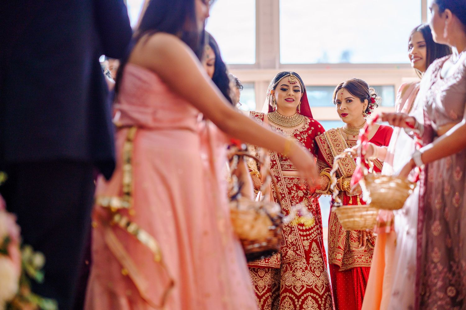 Wedding guests in pink and red traditional Indian attire dancing and celebrating at a reception.