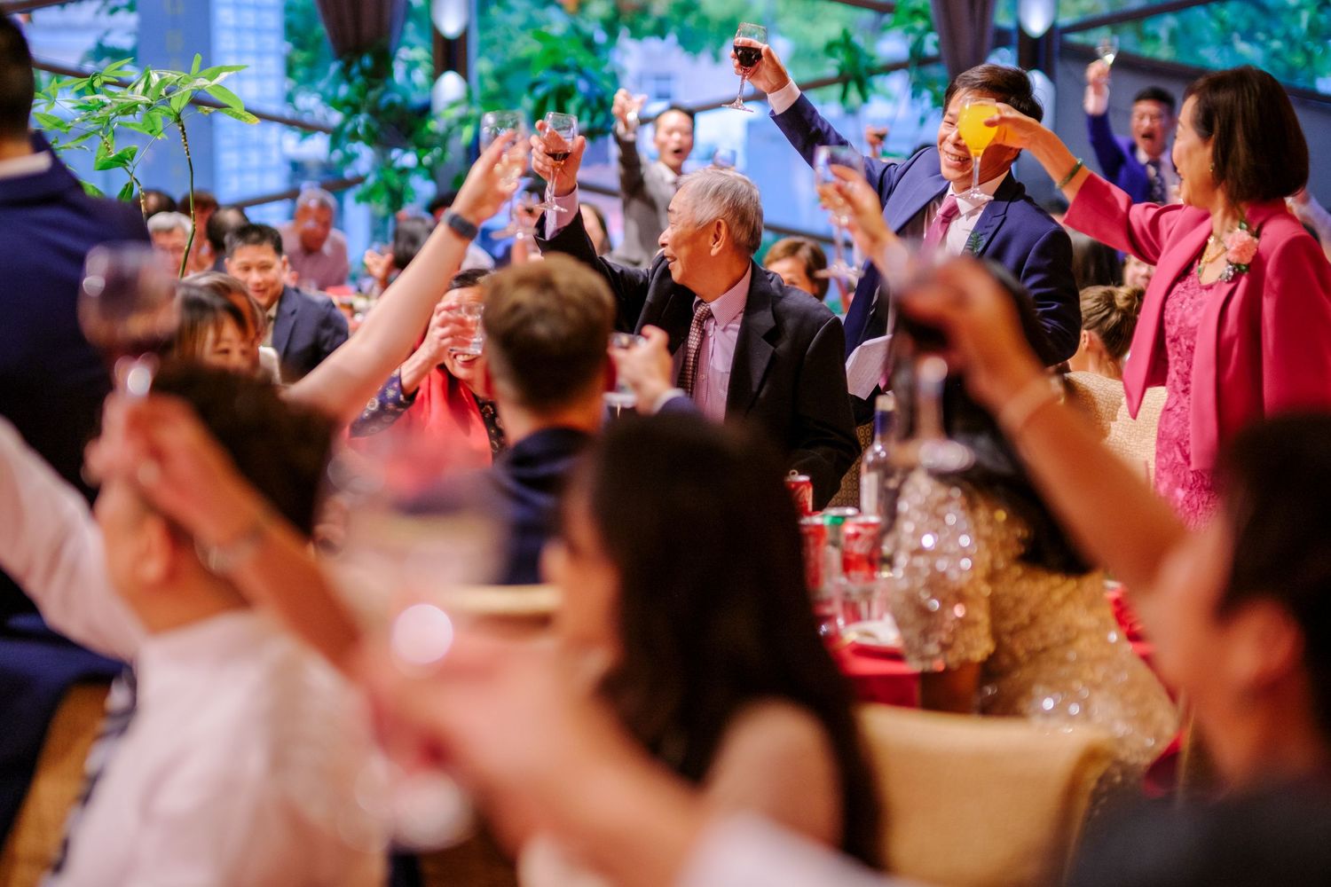 Wedding reception guests raise their glasses in a celebratory toast outdoors under a covered venue.
