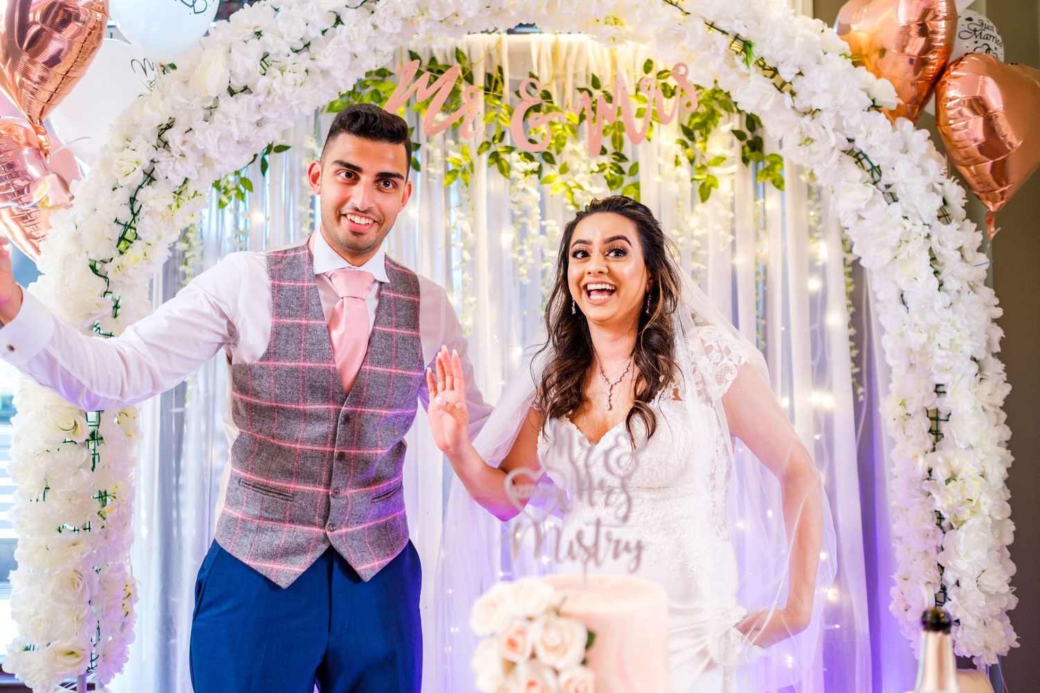 Wedding celebration under white floral arch with confetti falling during a joyous moment.