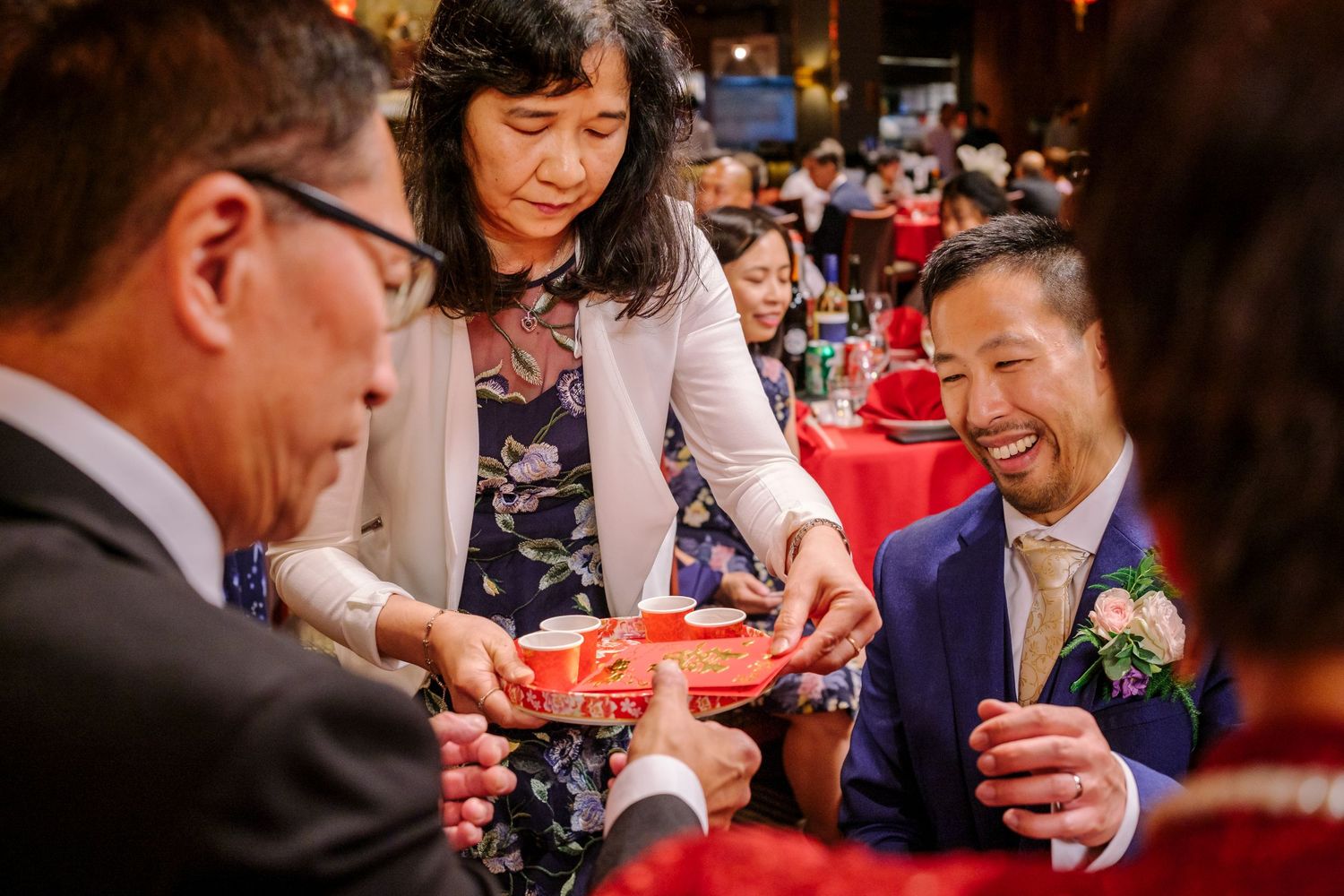 Wedding guests participate in a traditional Chinese tea ceremony with red cups and formal attire.