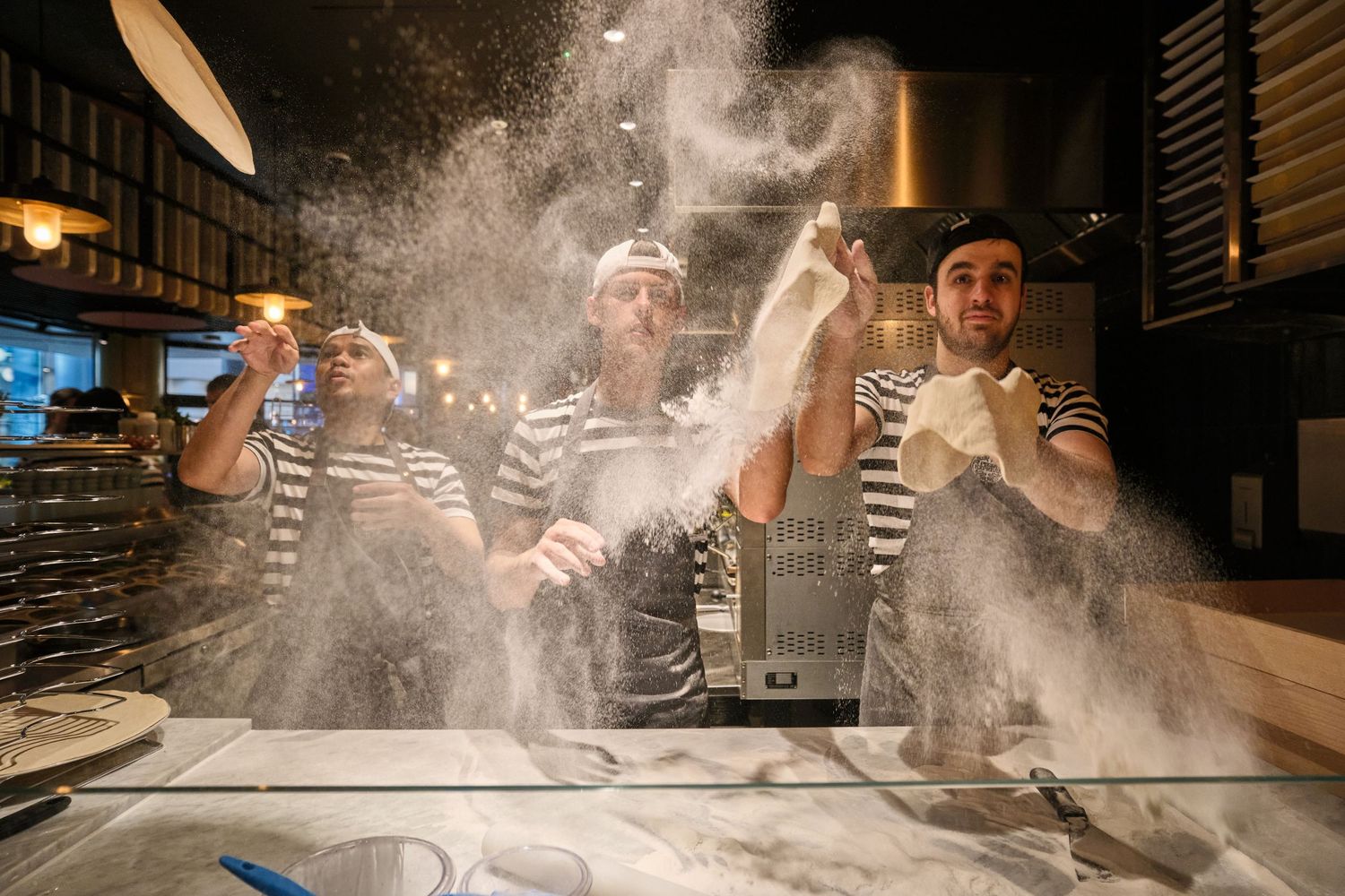 Flour dust flying dramatically during pizza dough preparation in restaurant kitchen.