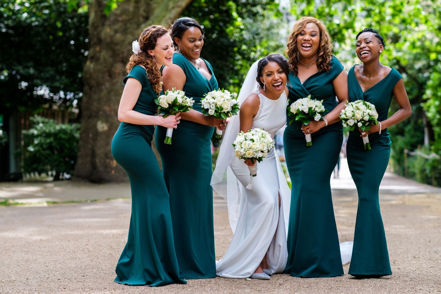Wedding party in emerald green dresses poses outdoors in a garden setting.