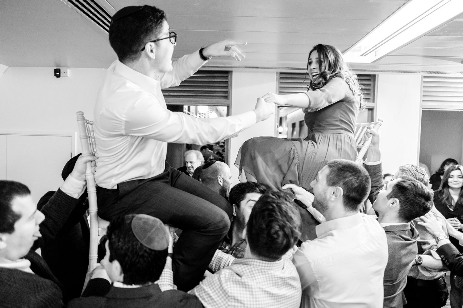 Dynamic black and white photo of people dancing and celebrating at a lively indoor event.