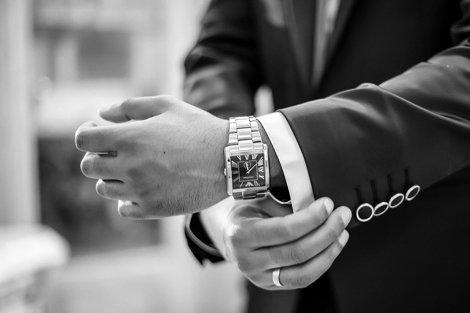 Close-up black and white shot of a formal watch and suit sleeve.
