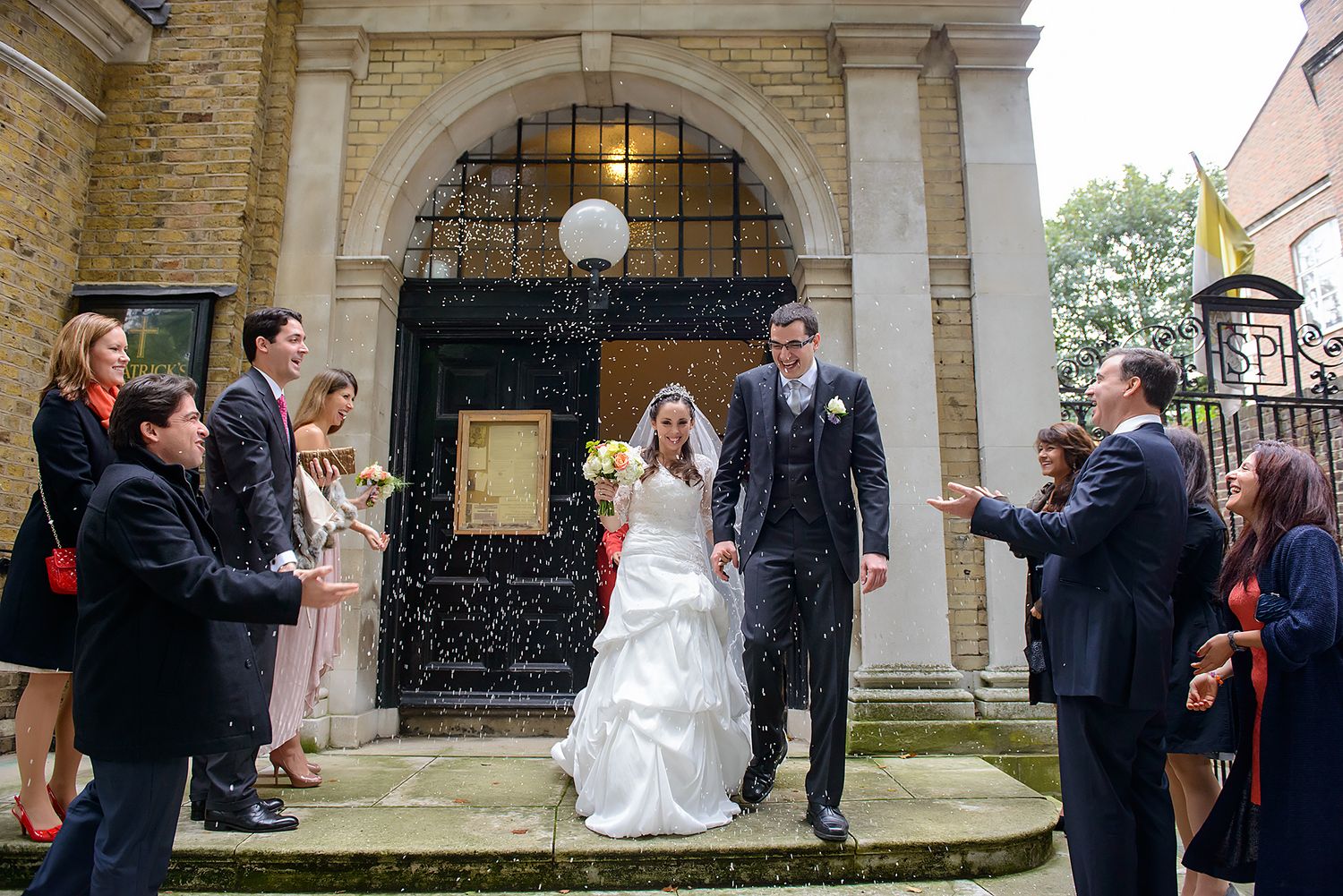 Wedding party gathered outside historic stone building with arched entrance.