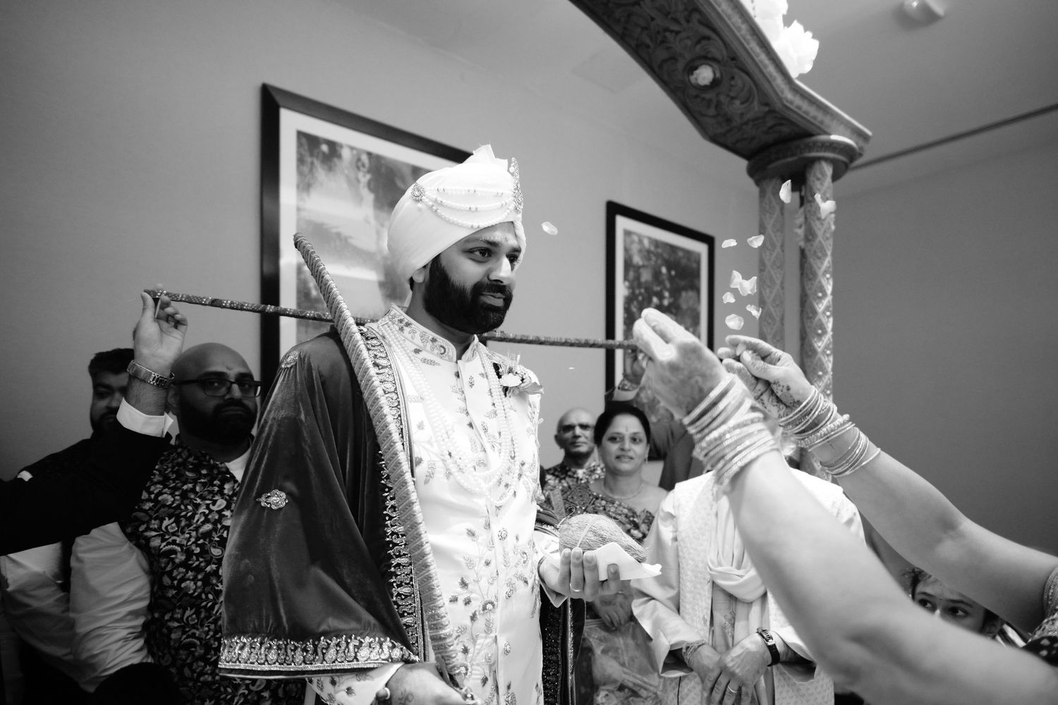 A joyful moment captured in black and white during a traditional Indian wedding celebration with guests looking on.