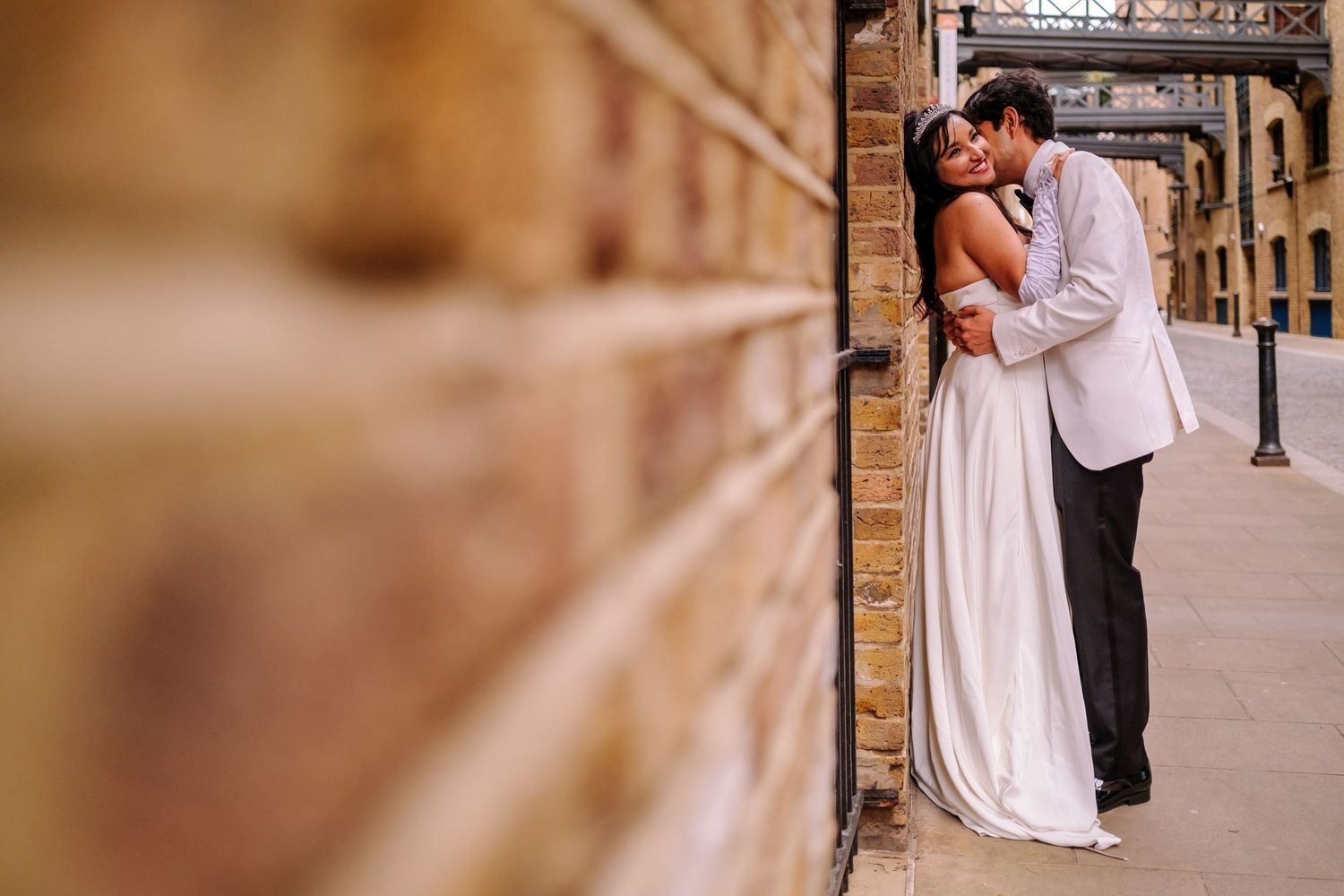 Artistic wedding portrait with soft focus brick wall and architectural details.