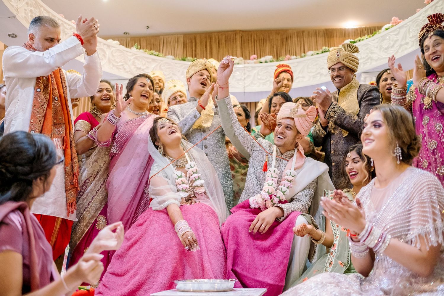 Wedding guests in vibrant pink and silver outfits celebrate joyfully during reception festivities.