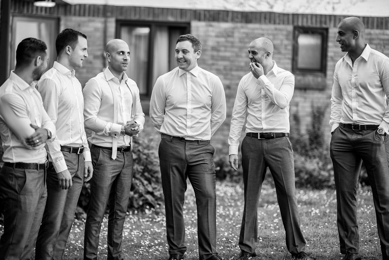 Groomsmen in matching gray suits and white shirts lined up outdoors.