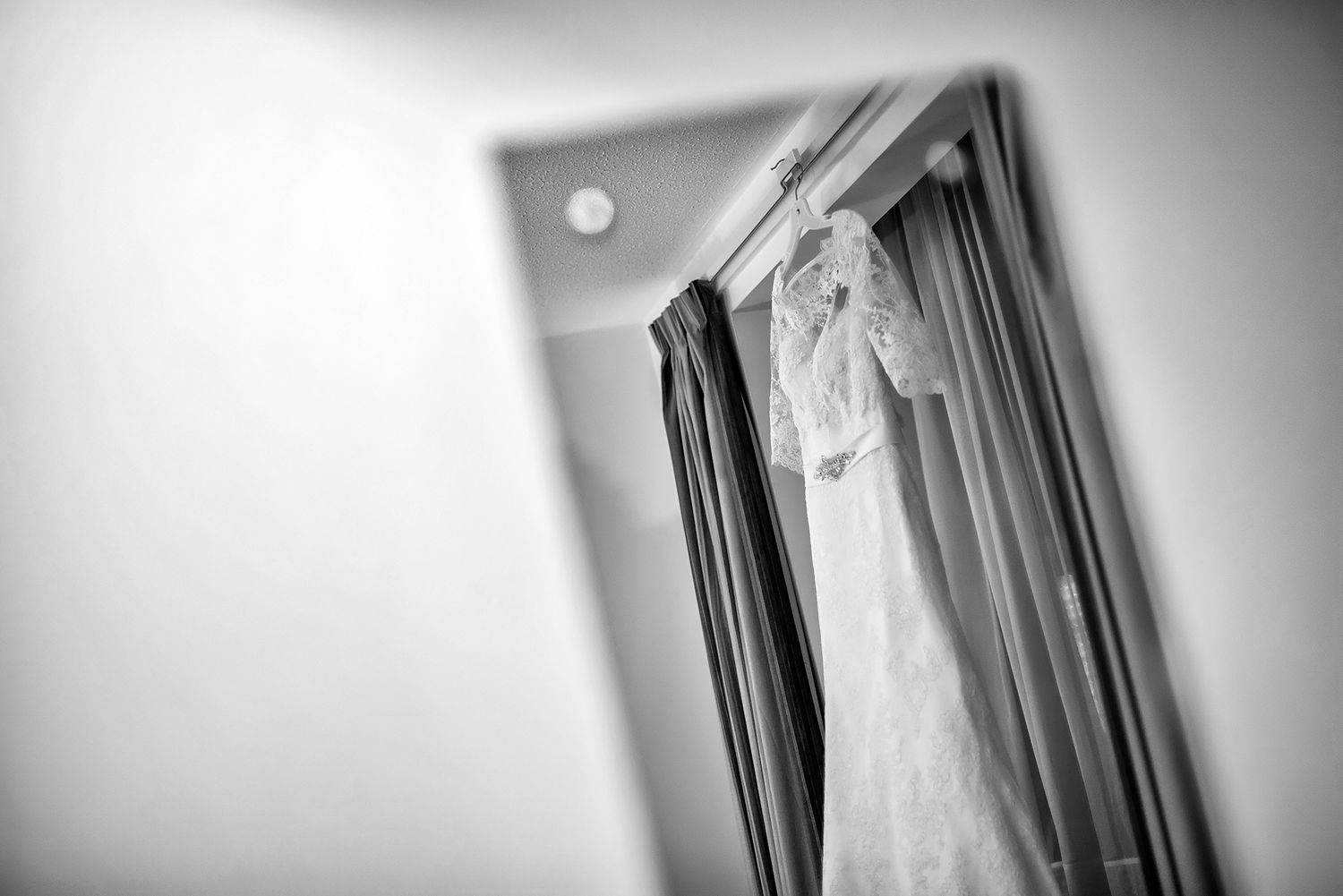White wedding dress hanging in soft focus creates ethereal bridal preparation scene.