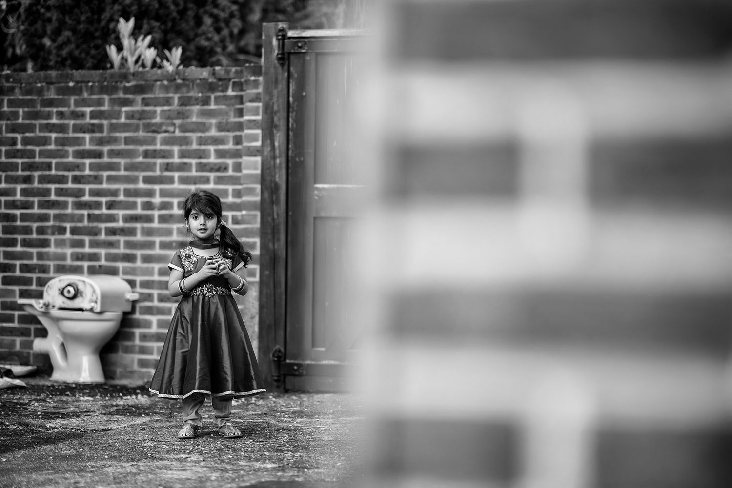 A figure plays in a garden against a brick wall background in black and white tones.