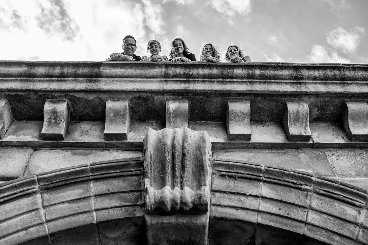 People sitting atop a stone architectural feature against cloudy sky in monochrome.